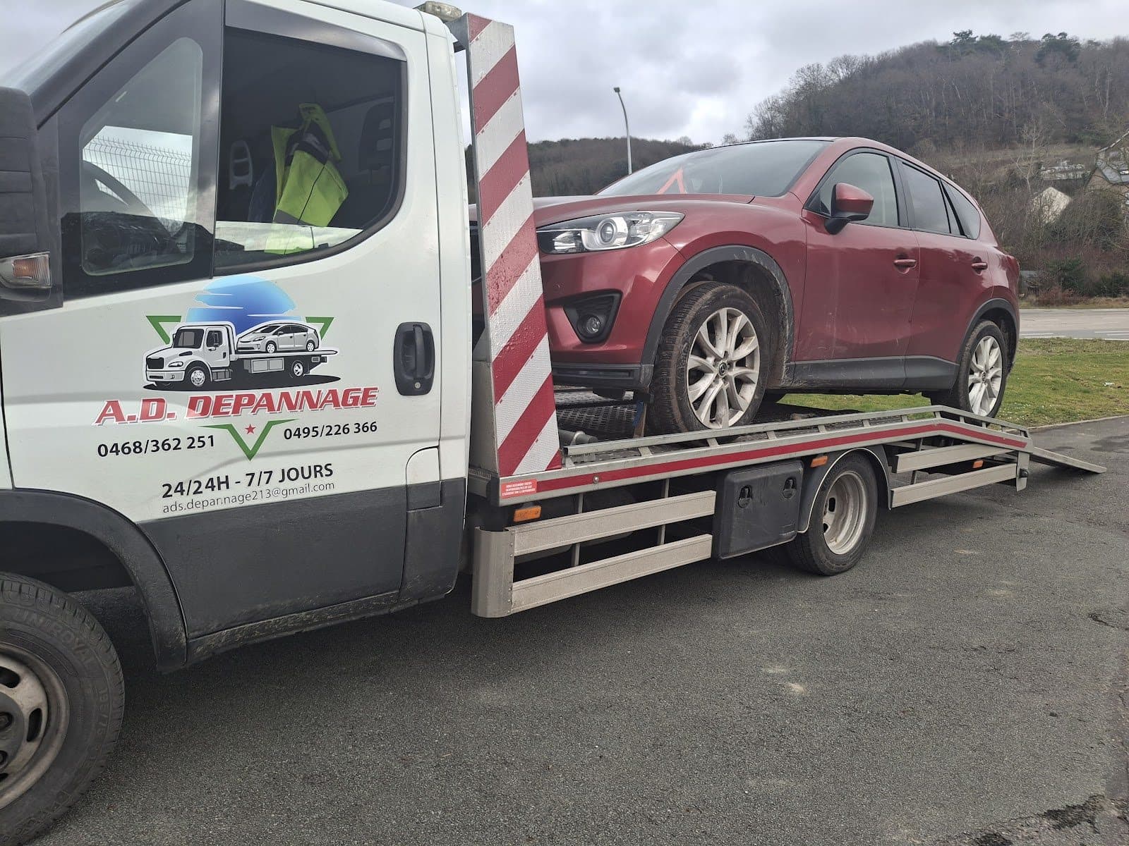 Un SUV Mazda rouge sur le plateau, la portière du camion au logo A.D. Dépannage