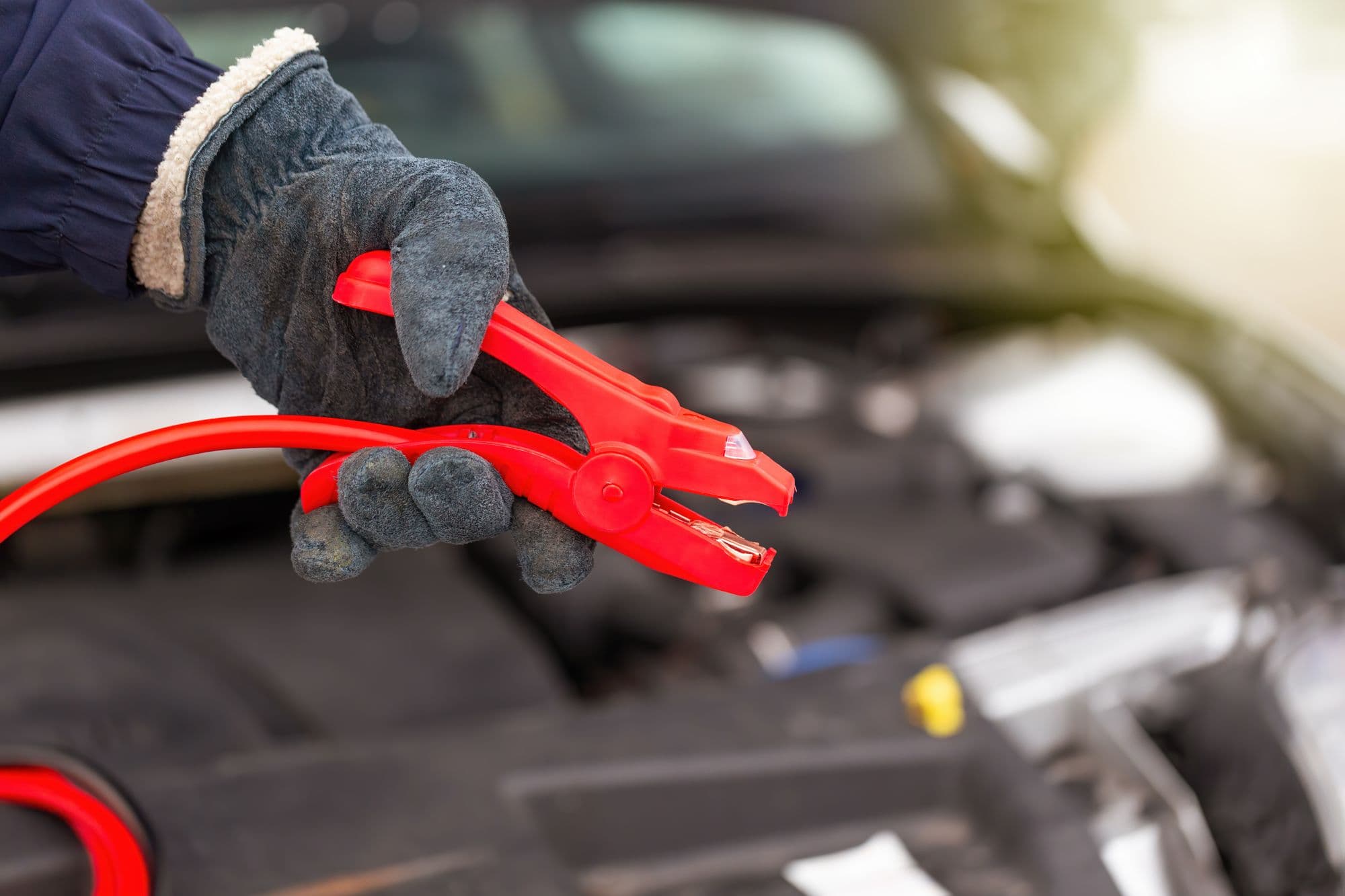 Une main tient la pince rouge d’un câble de démarrage près d’une voiture